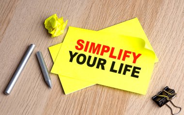 SIMPLIFY YOUR LIFE text on a yellow sticky on wooden background