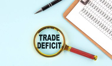 TRADE DEFICIT text on a magnifier with clipboard on blue background