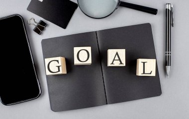 Word GOAL on wooden block on a black notebook with smartpone, credit card and magnifier