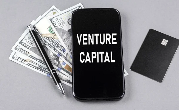 Credit card and text VENTURE CAPITAL on a smartphone with dollars and pen. Business concept