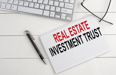 REAL ESTATE INVESTMENT TRUST text on notebook with keyboard , pen glasses on a white wooden background