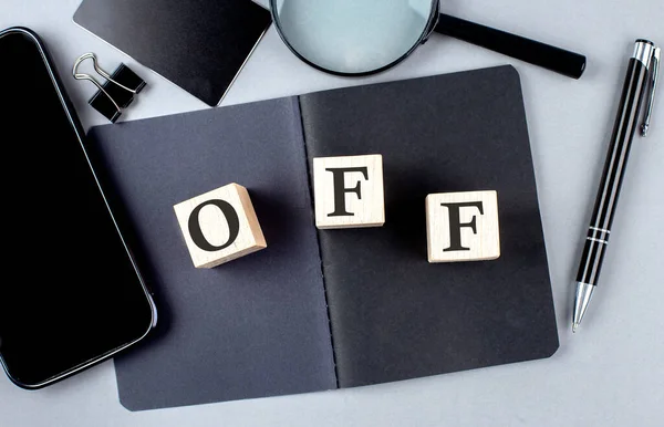 Word OFF on a wooden block on black notebook with smartpone, credit card and magnifier