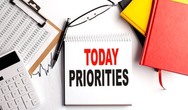 TODAY PRIORITIES text on notebook with clipboard and calculator on a white background