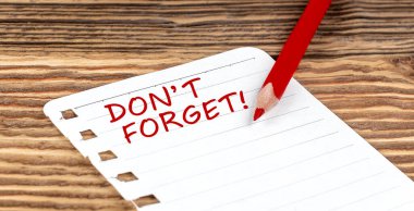 Word DON'T FORGET on paper with ped pencil on wooden background