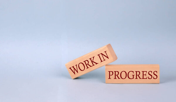 WORKS IN PROGRESS text on wooden block, blue background