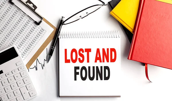 LOST AND FOUND text on notebook with clipboard and calculator on a white background