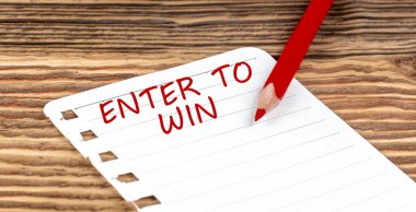 Word ENTER TO WIN on paper with ped pencil on wooden background