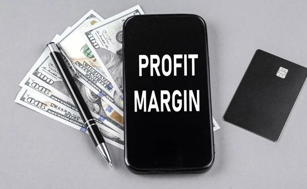 Credit card and text PROFIT MARGIN on smartphone with dollars and pen. Business