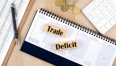 TRADE DEFICIT word written on a wooden block on planner with coins, clipboard and a calculator
