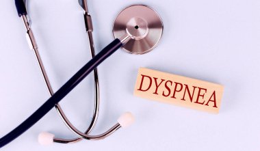 On a blue background, stethoscope and wooden block with the word DYSPNEA .Medical concept