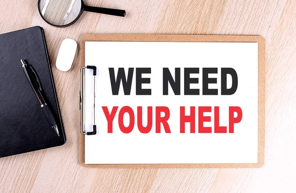 WE NEED YOUR HELP text on a clipboard on wooden background