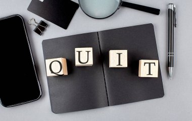Word QUIT on a wooden block on black notebook with smartpone, credit card and magnifier