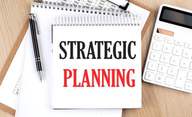 STRATEGIC PLANNING hesap makinesi, pano ve kalemin yanında beyaz not defteriyle yazılmıştır. İş konsepti