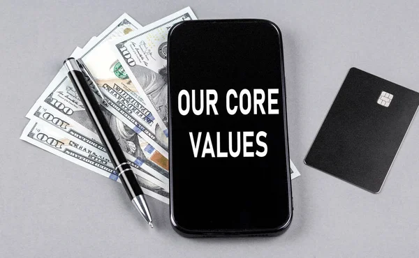 Credit card and text OUR CORE VALUES on a smartphone with dollars and pen. Business concept