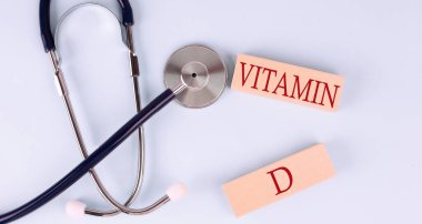 Mavi arka planda, steteskop ve VITAMIN D sözcüğüyle ahşap blok.
