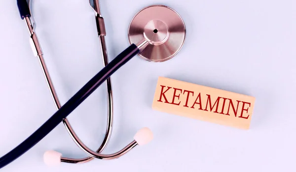 Mavi arka planda steteskop ve tahta blokta KETAMINE kelimesi var. Tıbbi kavram.