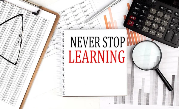 NEVER STOP LEARNING text on a notebook with clipboard and calculator on a chart background