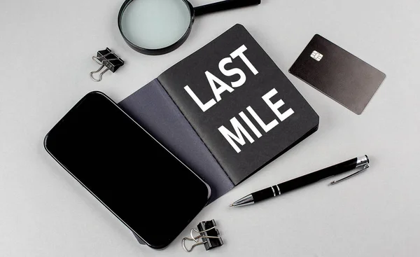 LAST MILE text written on a black notebook with smartphone, magnifier and credit card