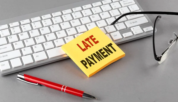 LATE PAYMENT text on sticky with keyboard, pen glasses on grey background