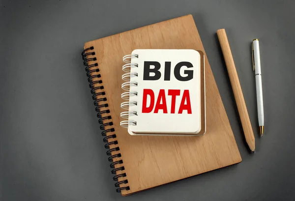 BIG DATA text on a notebook with pen and pencil on grey background
