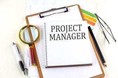 Beyaz zemin üzerinde pano olan bir defter üzerindeki PROJECT MANAGER metni