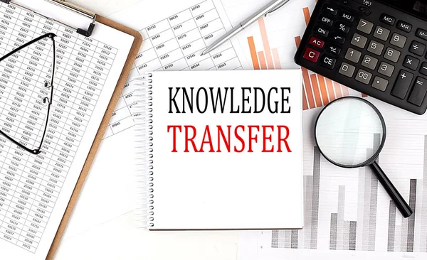 KNOWLEDGE TRANSFER text on a notebook with clipboard and calculator on a chart background