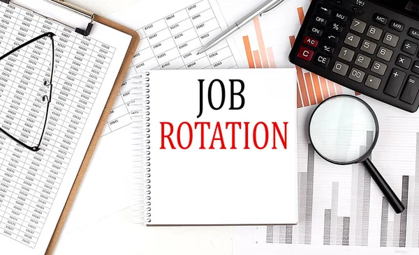 Stock image JOB ROTATION text on a notebook with clipboard and calculator on a chart background