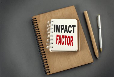 Gri arkaplanda kalem ve kalemle bir dizüstü bilgisayarda IMPACT FACTOR metni