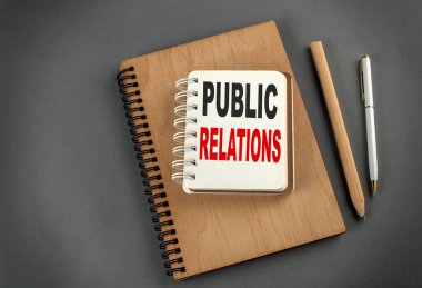 Gri zemin üzerinde kalem ve kalem bulunan bir defter üzerindeki PUBLIC İlişkileri metni