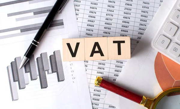 stock image VAT text on a wooden block on graph background with pen and magnifier