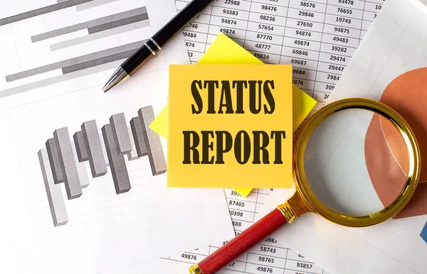 STATUS REPORT text on sticky on the graph background with pen and magnifier