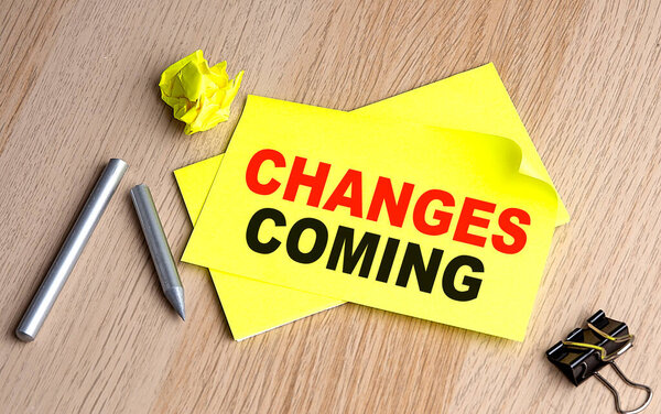 CHANGES COMING text on a yellow sticky on wooden background