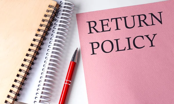 RETURN POLICY word on pink paper with office tools on white background