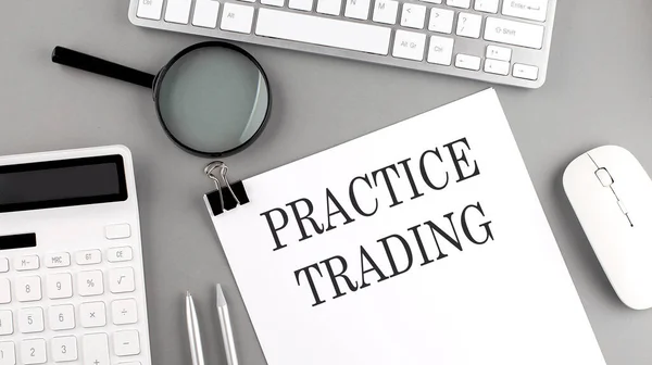 PRACTICE TRADING written on paper with office tools and keyboard on grey background