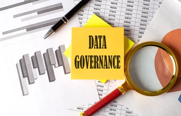DATA GOVERNANCE text on sticky on the graph background with pen and magnifier