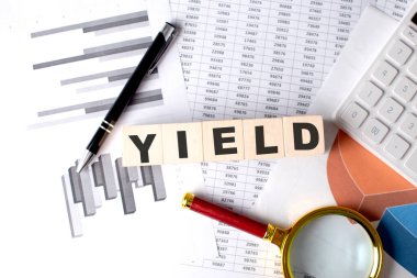 Grafik arkaplanındaki tahta blokta kalem ve büyüteçle YIELD metni