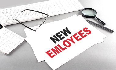 NEW EMPLOYEES hesap makinesi ve beyaz klavyenin yanındaki gri arkaplan üzerine bir kağıt üzerinde metin