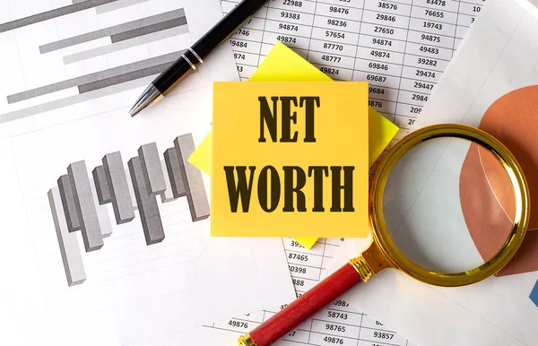 NET WORTH text on sticky on the graph background with pen and magnifier