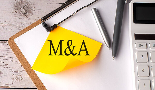M and A word on a yellow sticky with calculator, pen and clipboard