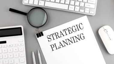 Ofis araçları ve gri arkaplanda klavye ile kağıda yazılmış STRATEGIC PLANNING