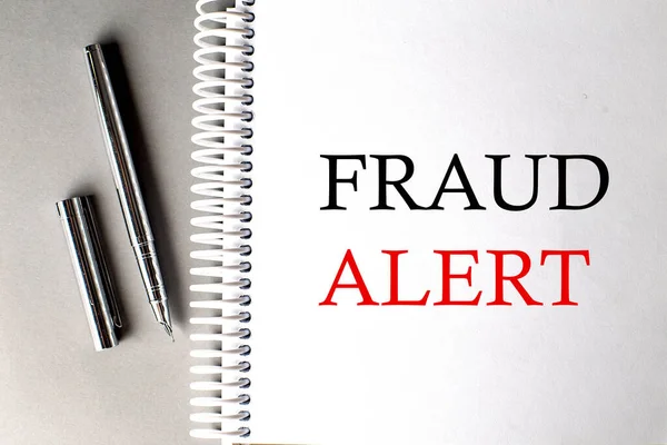FRAUD ALERT text on notebook with pen on grey background