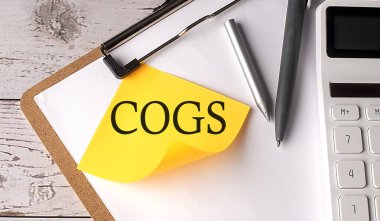 Hesap makinesi, kalem ve pano ile sarı yapışkan üzerinde COGS sözcüğü