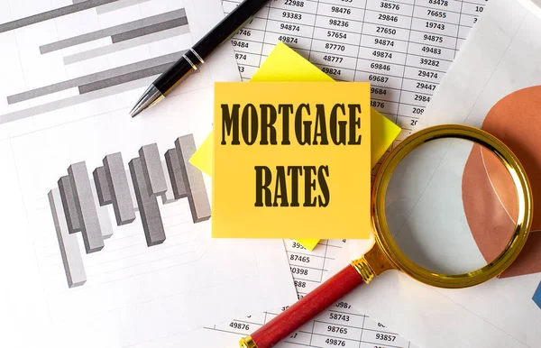 MORTGAGE RATES text on sticky on the graph background with pen and magnifier
