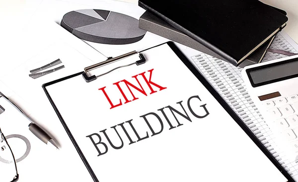 LINK BUILDING text on a paper clipboard with chart and notebook on withe background