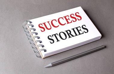 Gri arkaplandaki bir defterde SUCCESS STORIES sözcüğü