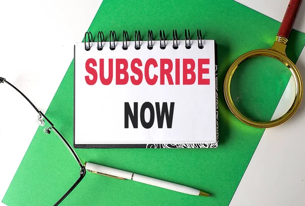 SUBSCRIBE NOW text on a notebook on green paper