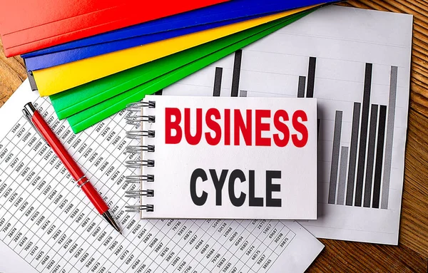 BUSINESS CYCLE text on a notebook with pen, folder on a chart background
