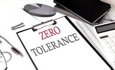 ZERO TOLERANCE arkaplan üzerinde çizelge ve not defteri olan bir kağıt pano üzerinde metin