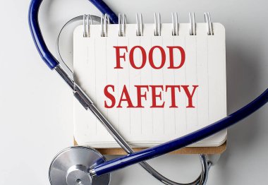 Arka planda tıbbi ekipman olan bir defterde yiyecek güvenliği kelimesi var.