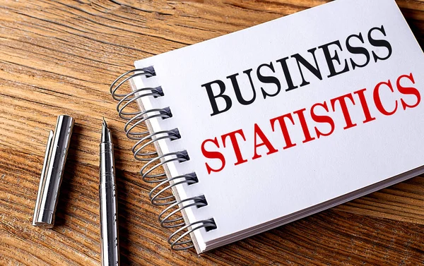 BUSINESS STATISTICS text on a notebook with pen on wooden background